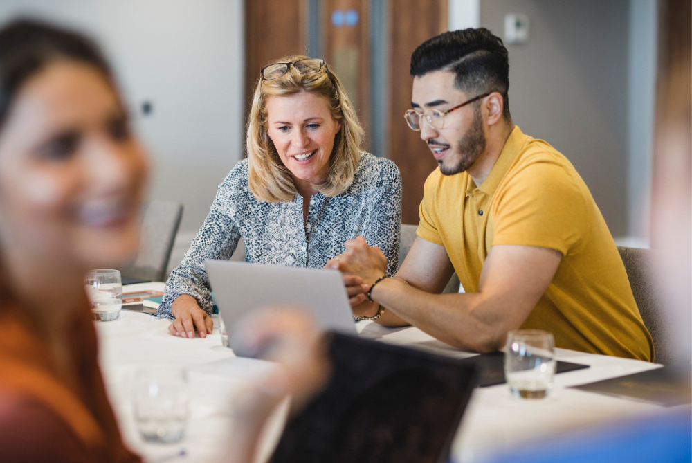 Two professionals - one man and one women - collaborating together on a laptop. 