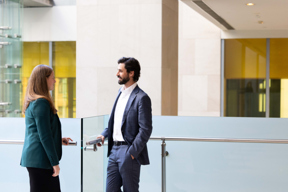 Man and woman in business attire standing in a hall way with white tones