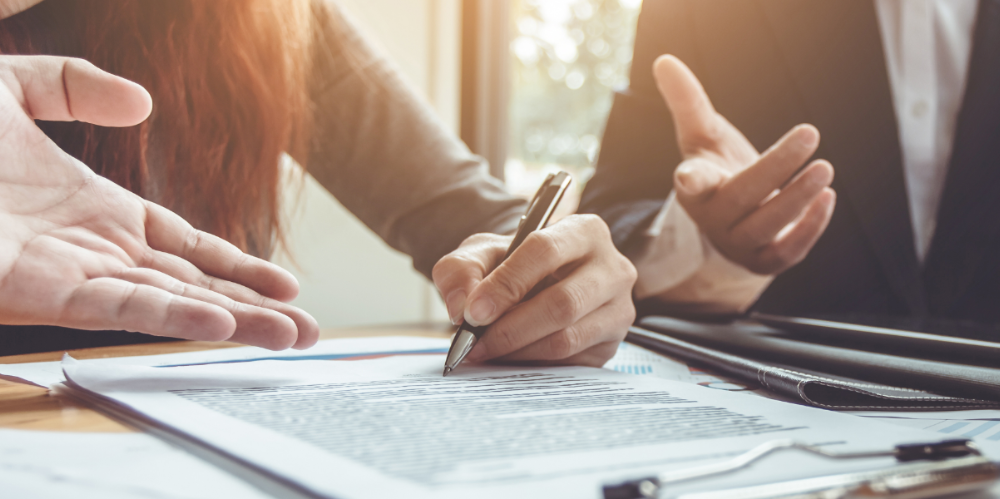 Close-up shot of three people sitting at a table, showing three sets of hands gesturing and writing on a clipboard.