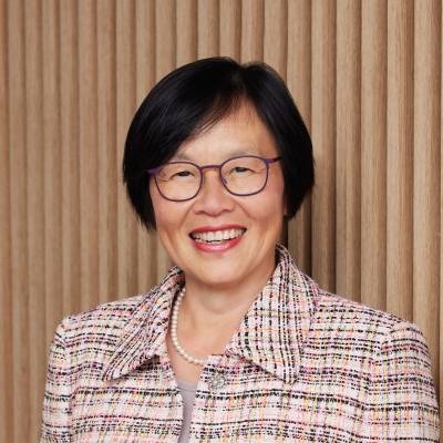 Women with short dark hair and glasses, smiling at camera with coloured knitted jacket and pearls on