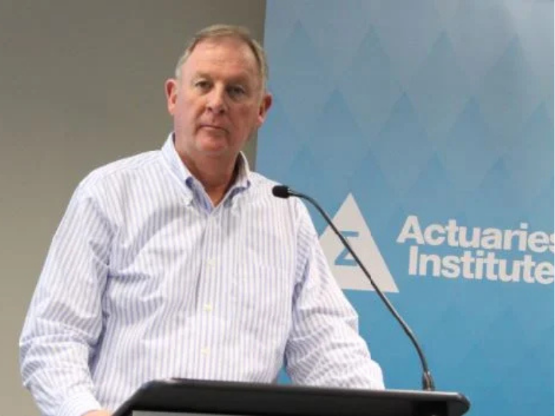 A man stands at a podium with an Actuaries Institute banner visible behind him.
