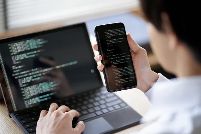 A man worker on coding on his phone and laptop.
