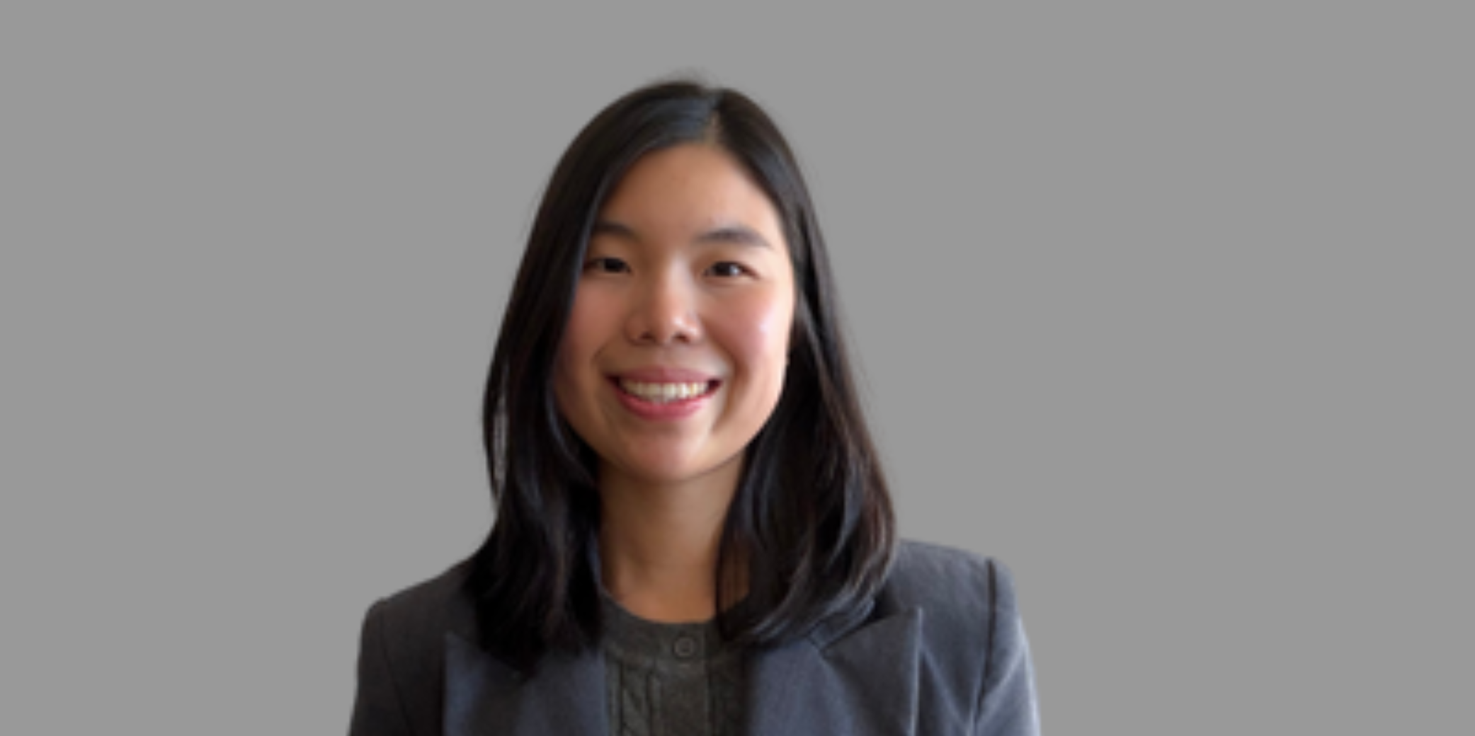 Female with long black hair smiling at camera with black shirt and grey background