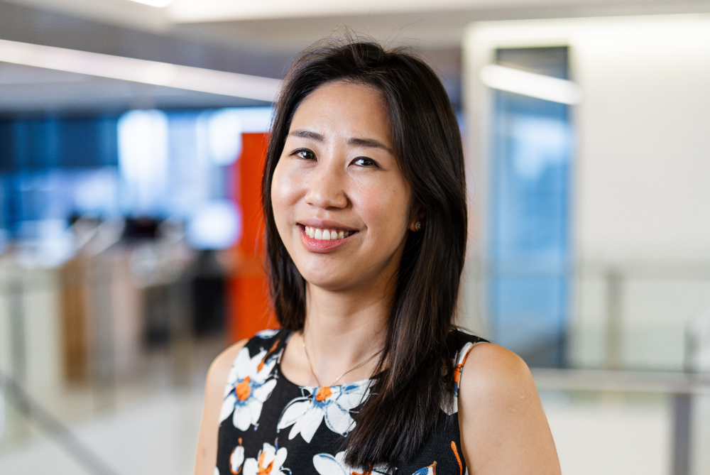 Portrait photo of woman smiling, shouder length black hair and black dress with large white flowers.