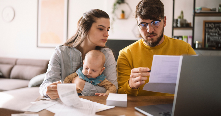 Couple with baby reviewing household bills and a laptop at the kitchen table.