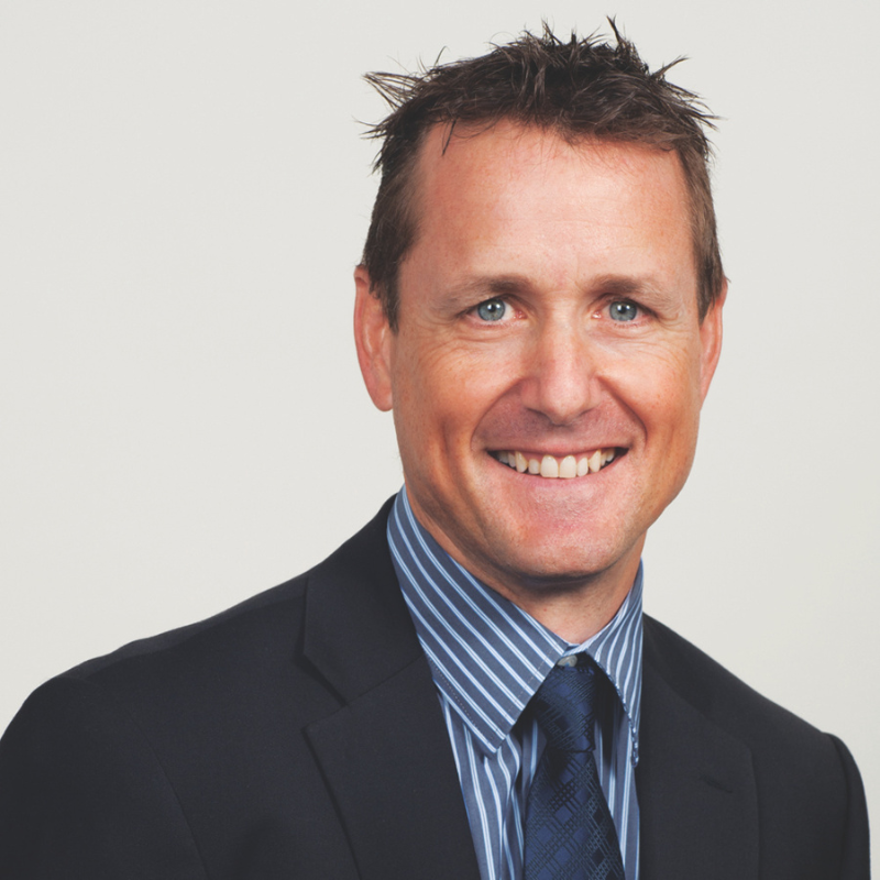 Portrait photo of Tim Andrew with dark suit, blue tile, and blue striped shirt