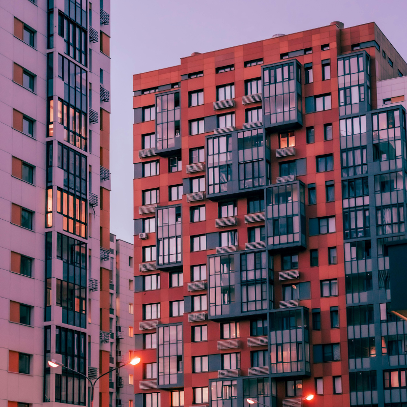 A cluster of apartment buildings in the evening, with street lights lit up.
