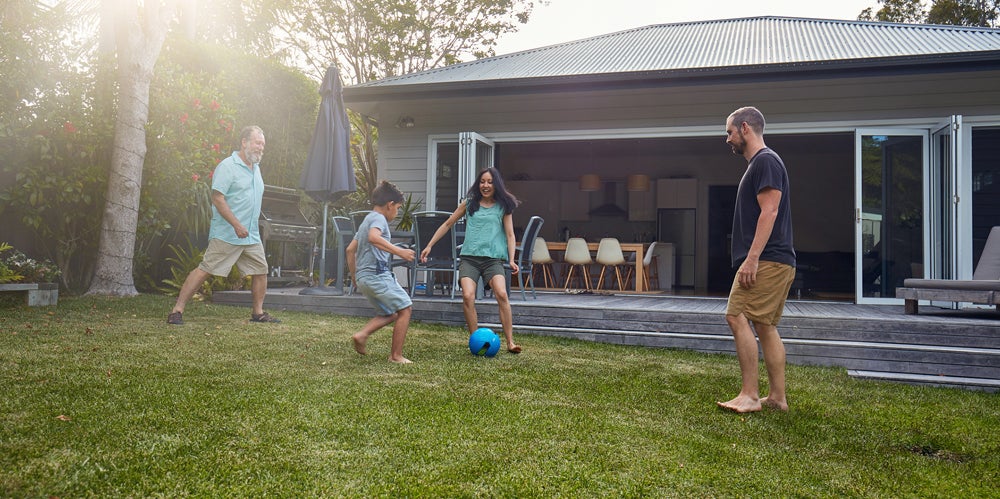 Two dads and two kids playing with a soccer ball in a backyard.