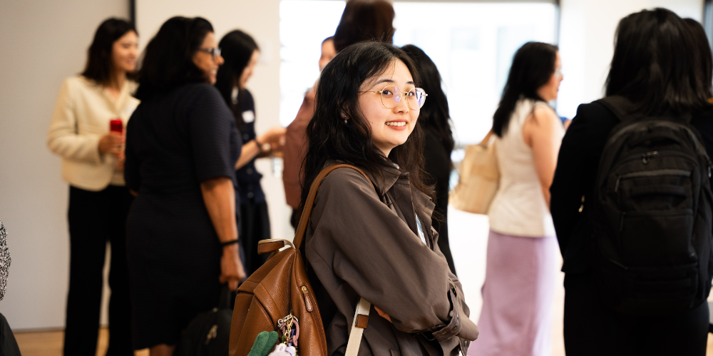 Women standing smiling at an event with people congregating in the hallway