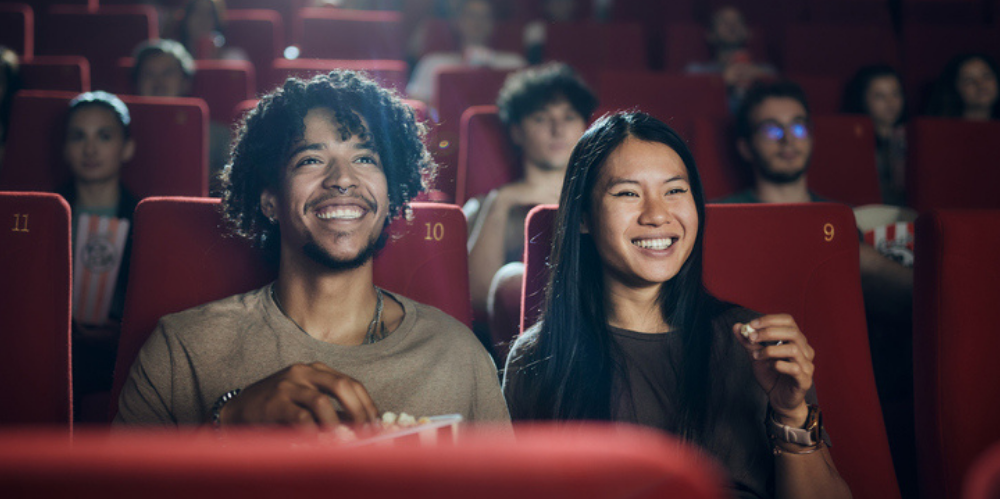 Happy diverse couple enjoying in their snack while watching a movie in theatre.