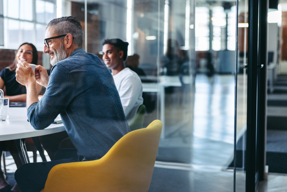 A close-up of an older man having a meeting with colleagues in a relaxed, office environment. 