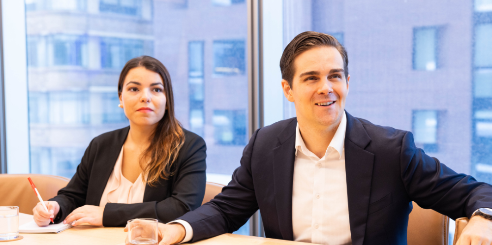 Two younger business people sitting in an office looking off camera with dark jackets and light coloured shirts
