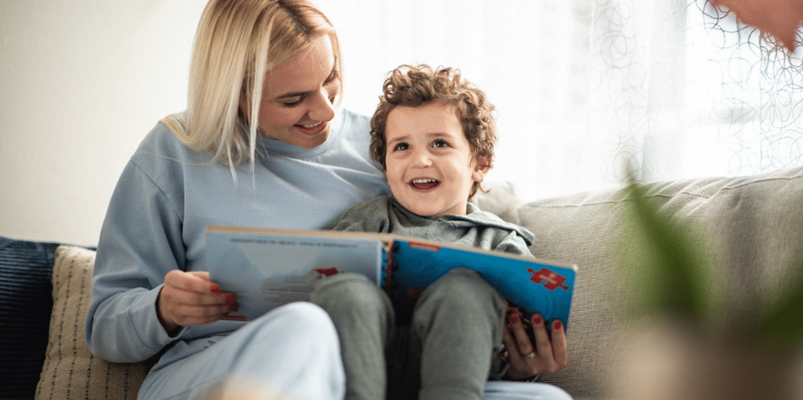 Mother sitting on lounge reading book to young son.