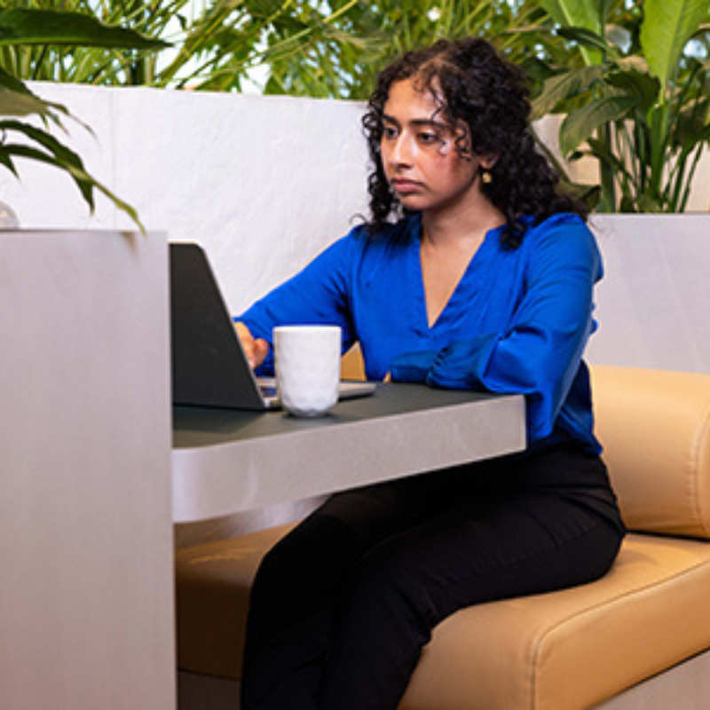 Young women dressed in a blue work shirt and black trousers sitting at a computer in a booth and reading