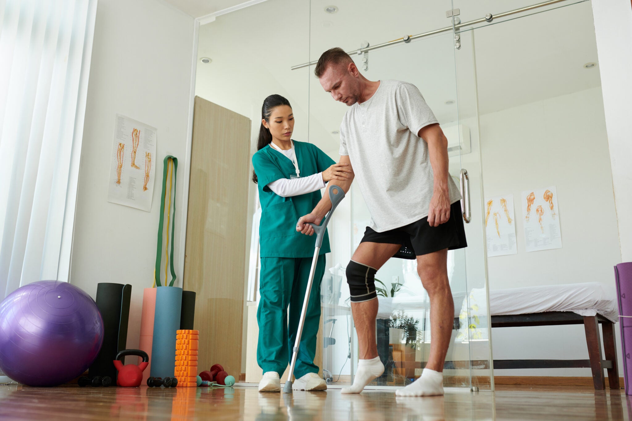 Nurse supporting patient learning to step on hurt leg leaning on crutch