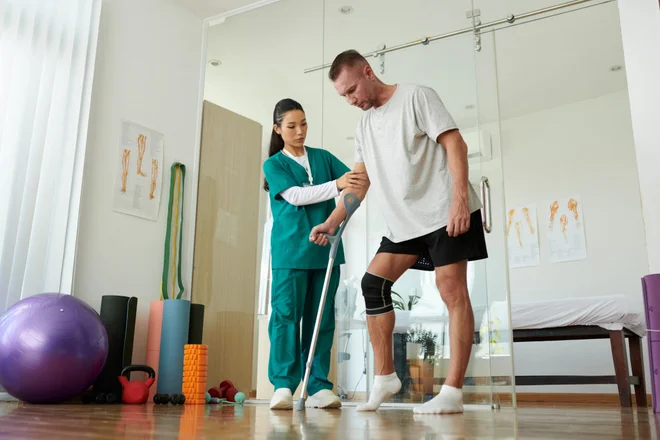 Nurse supporting patient learning to step on hurt leg leaning on crutch