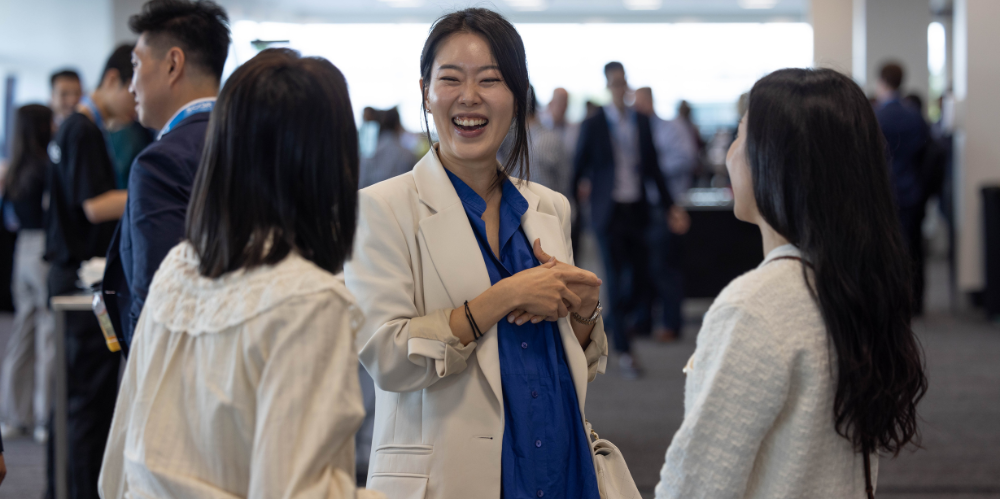 Three professional women talking and laughing in a crowded room.