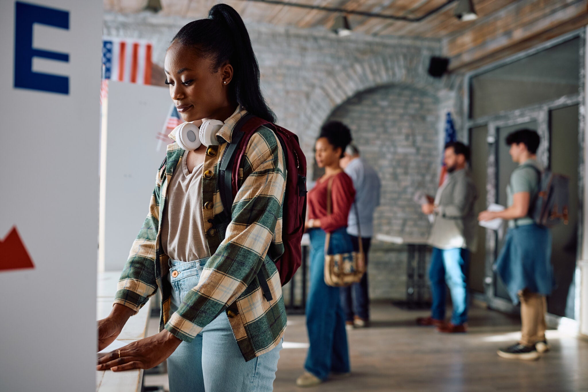 Young African American female citizen voting at polling place during US elections.