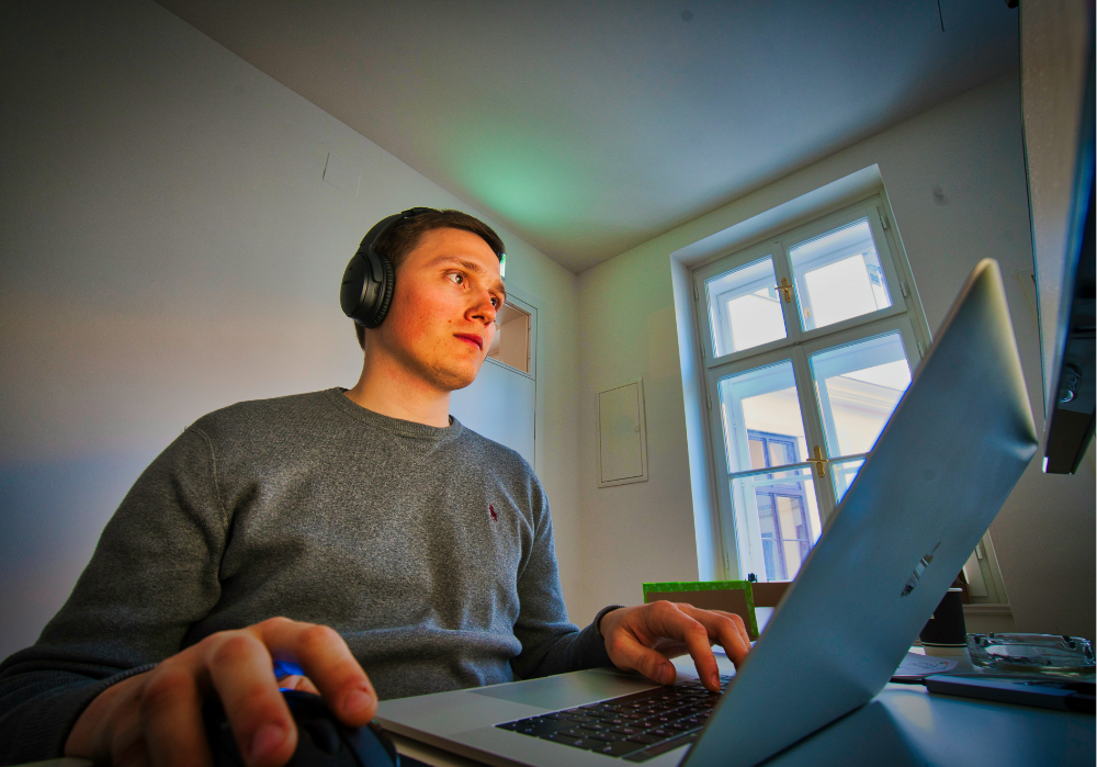 A mid-20s man with headphones on, working on his laptop. 
