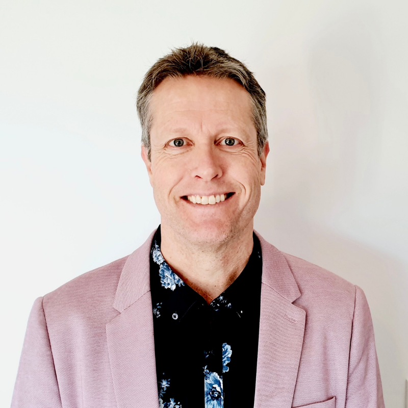 Man smiling at camera with a mauve jacket and black shirt