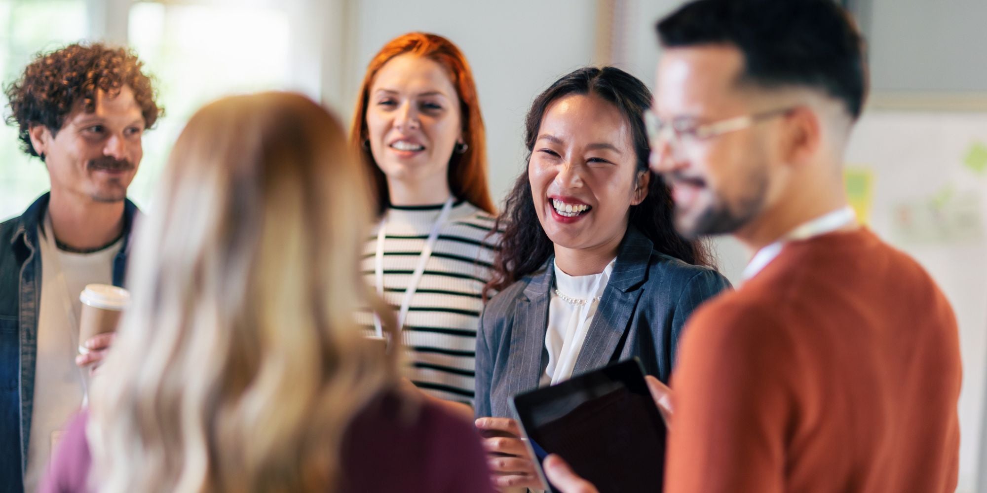 Group of men and women at conference standing and talking to each other and laughing.