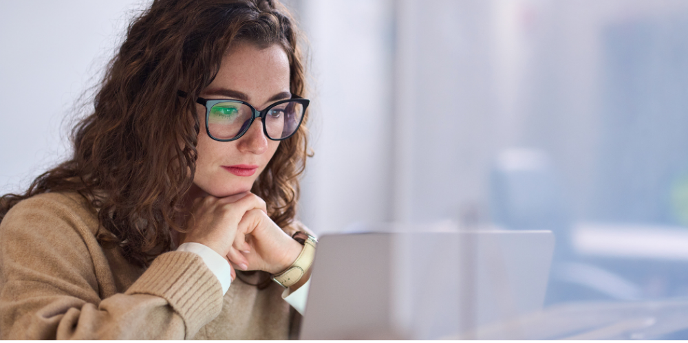 Young professional woman wearing glasses using laptop watching online webinar or training web course, looking at computer, thinking, doing research.