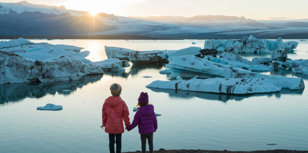 Children holding hands watching the sun rise over an icy terrain