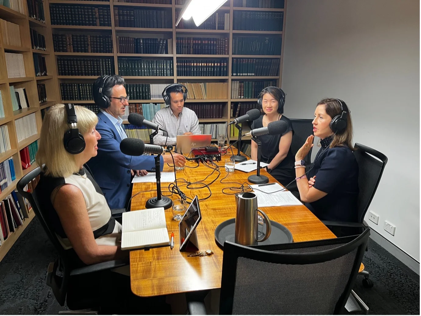 people sit around table wearing headphones, recording a podcast
