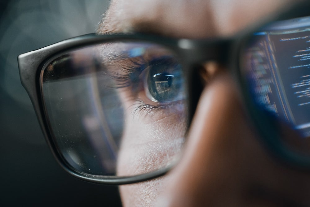 Close up of man wearing glasses with reflection of code in background