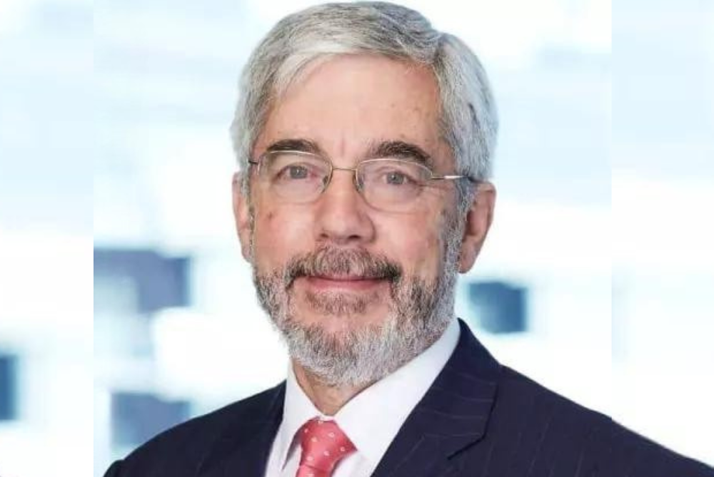 Business man with white hair, grey beard and navy suit with white shirt and red tie, wearing glasses.