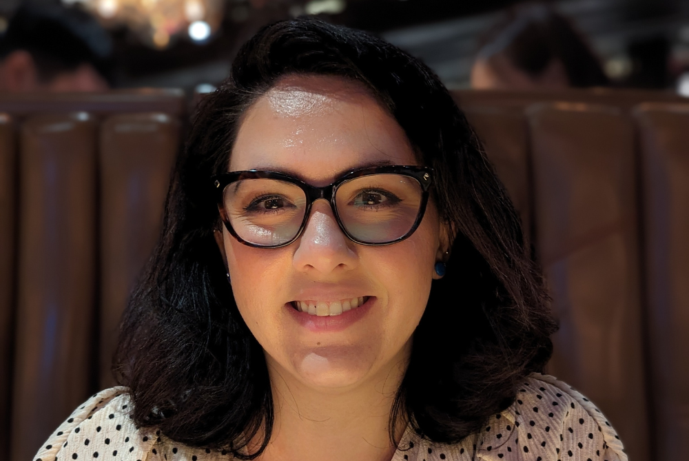 Portrait photo of women smiling with dark hair to shoulder, glasses and white blouse with black dots.