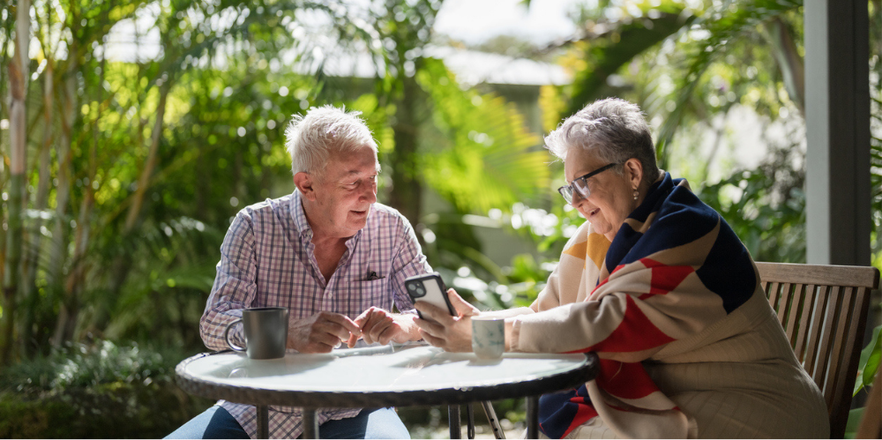 Two older people sitting at table looking at phone.