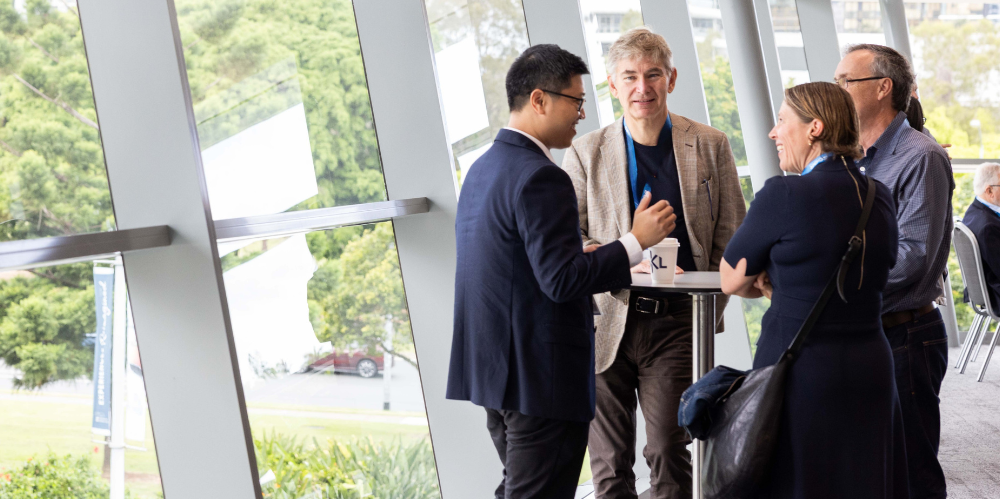 Group of business people talking around a table near a floor to ceiling window.