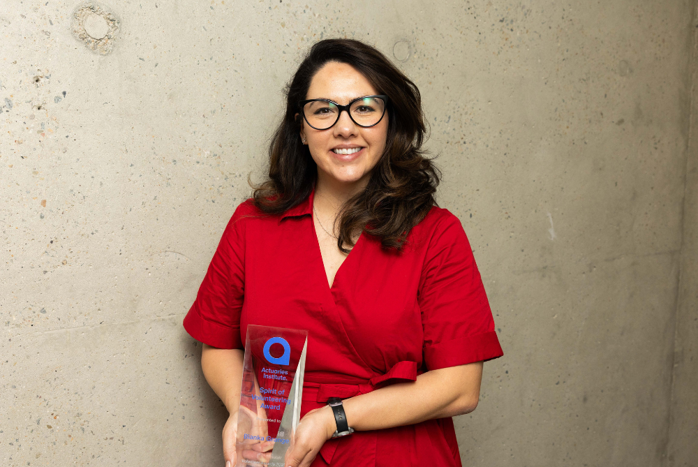 Business women in red dress and black glasses and hair looking at camera, smiling and holding a trophy at waist