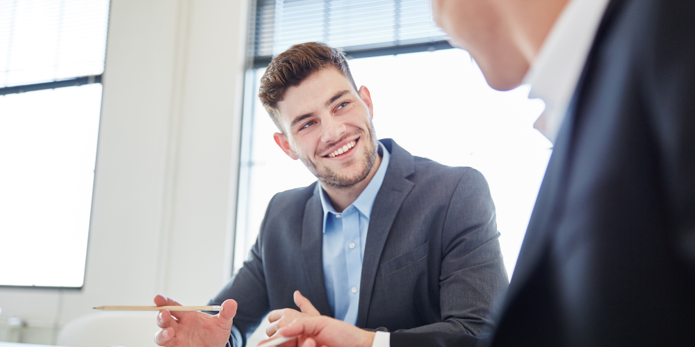 Man in office talking to a colleague, sitting at a table
