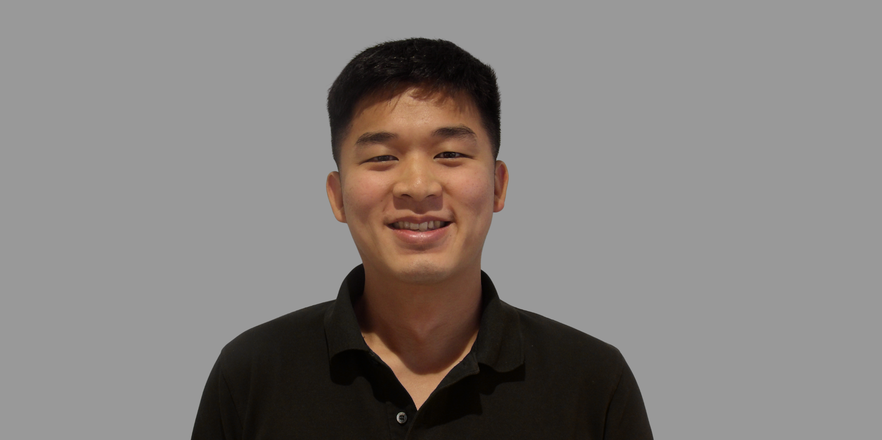Male smiling with black hair with black shirt and grey background