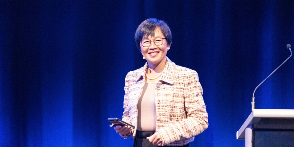 women on stage smiling and presenting with mobile in hand 