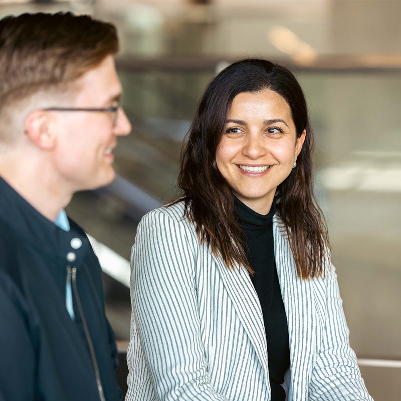 A man with glasses and a woman with brown hair and a striped blazer talking at event