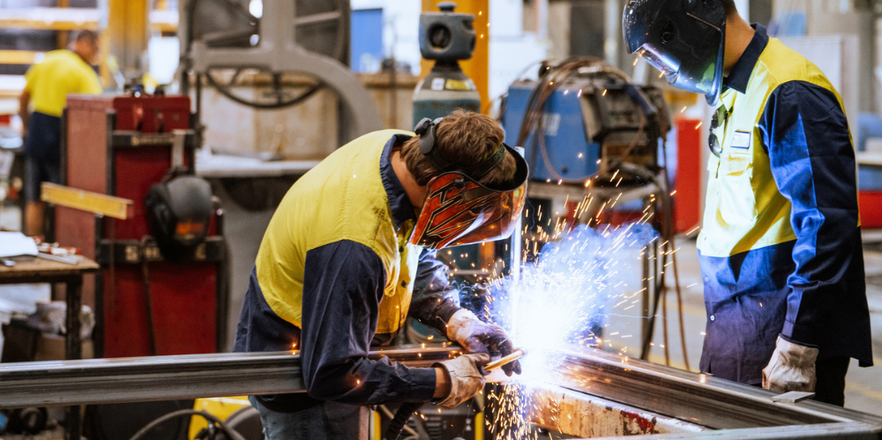Worker in protective gear welding metal in an industrial factory setting.