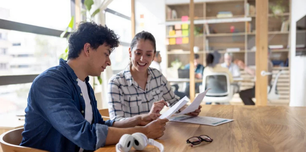 Two colleagues reviewing a document together at a desk in a bright, open-plan office