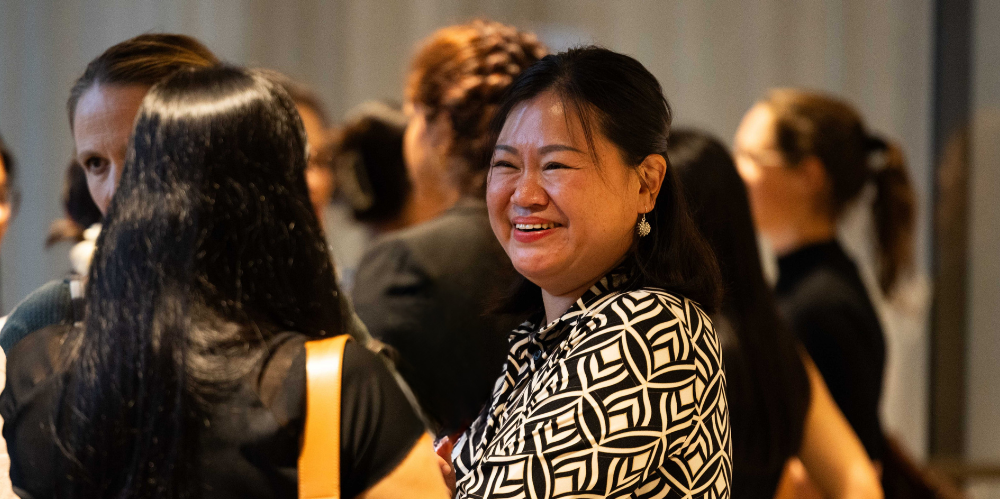 Female smiling and talking to a colleague at an event, dark hair and black and white geometric striped dress.