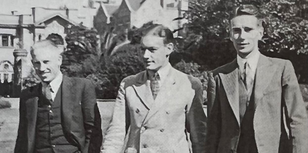 Black and white, vintage image of three men in suits standing outside.