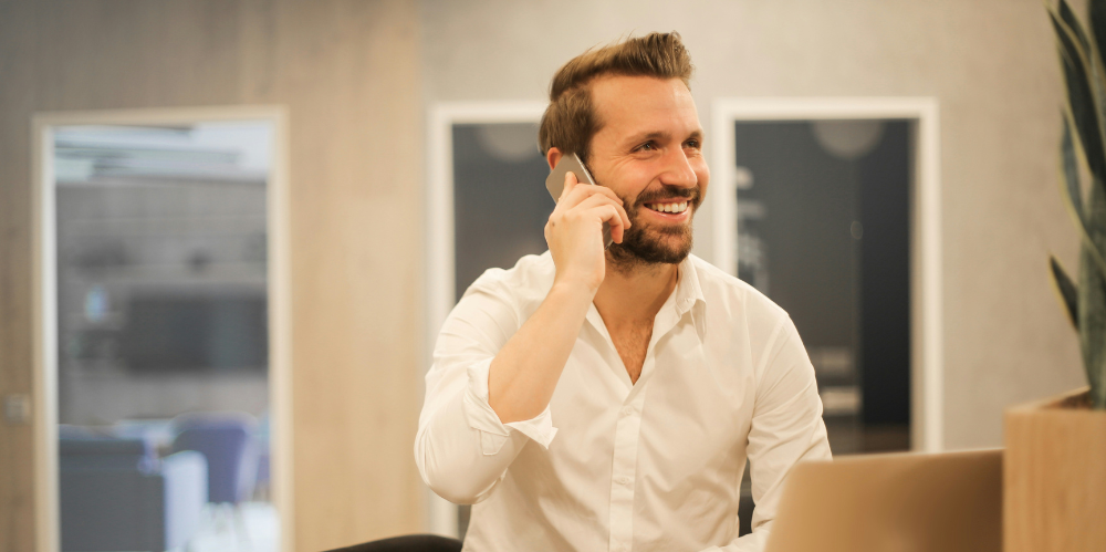 Business man smiling and talking on the phone, in a white shirt.