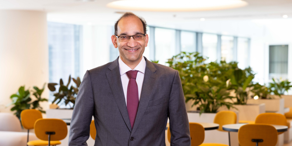 Business man in grey business suit and mauve tie in office with yellow chairs in background