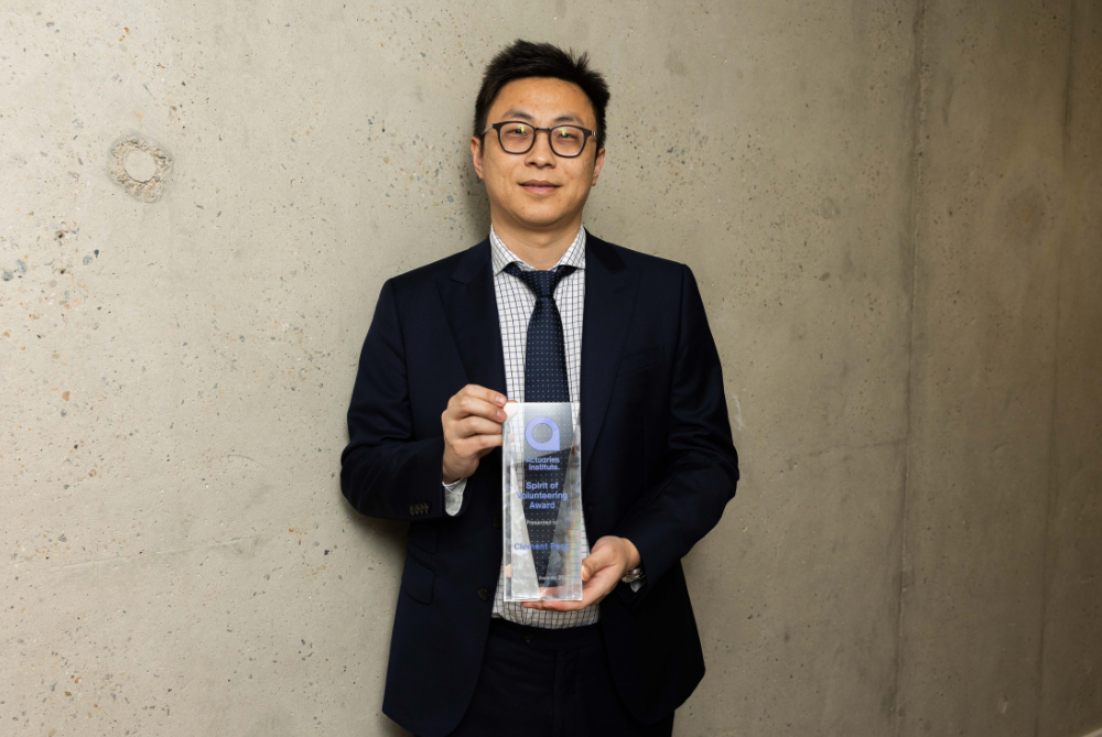 Business man with dark hair and glasses, with suit and tie, holding trophy and looking straight at camera