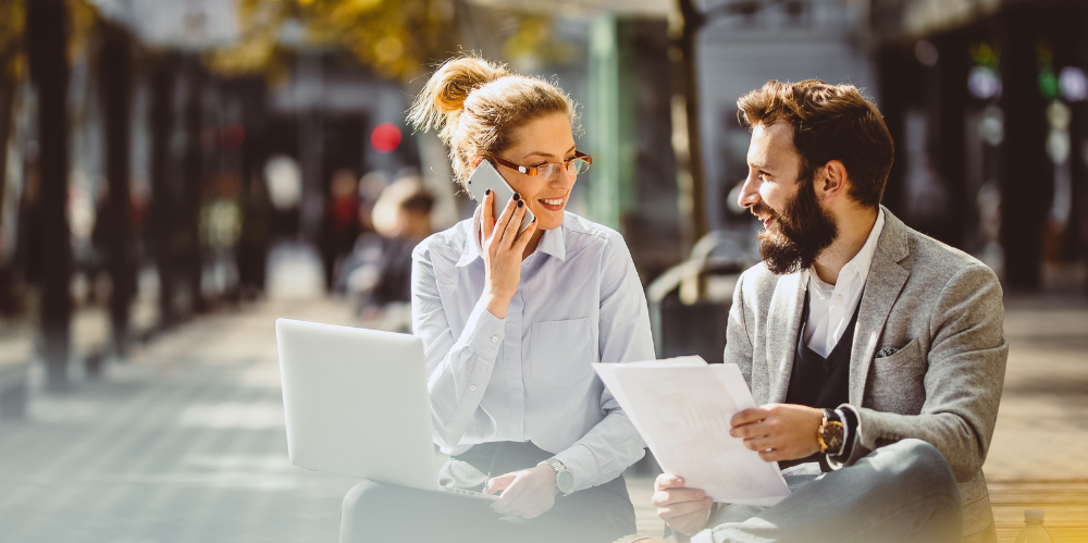 Woman talking on phone sitting with man holding papers.