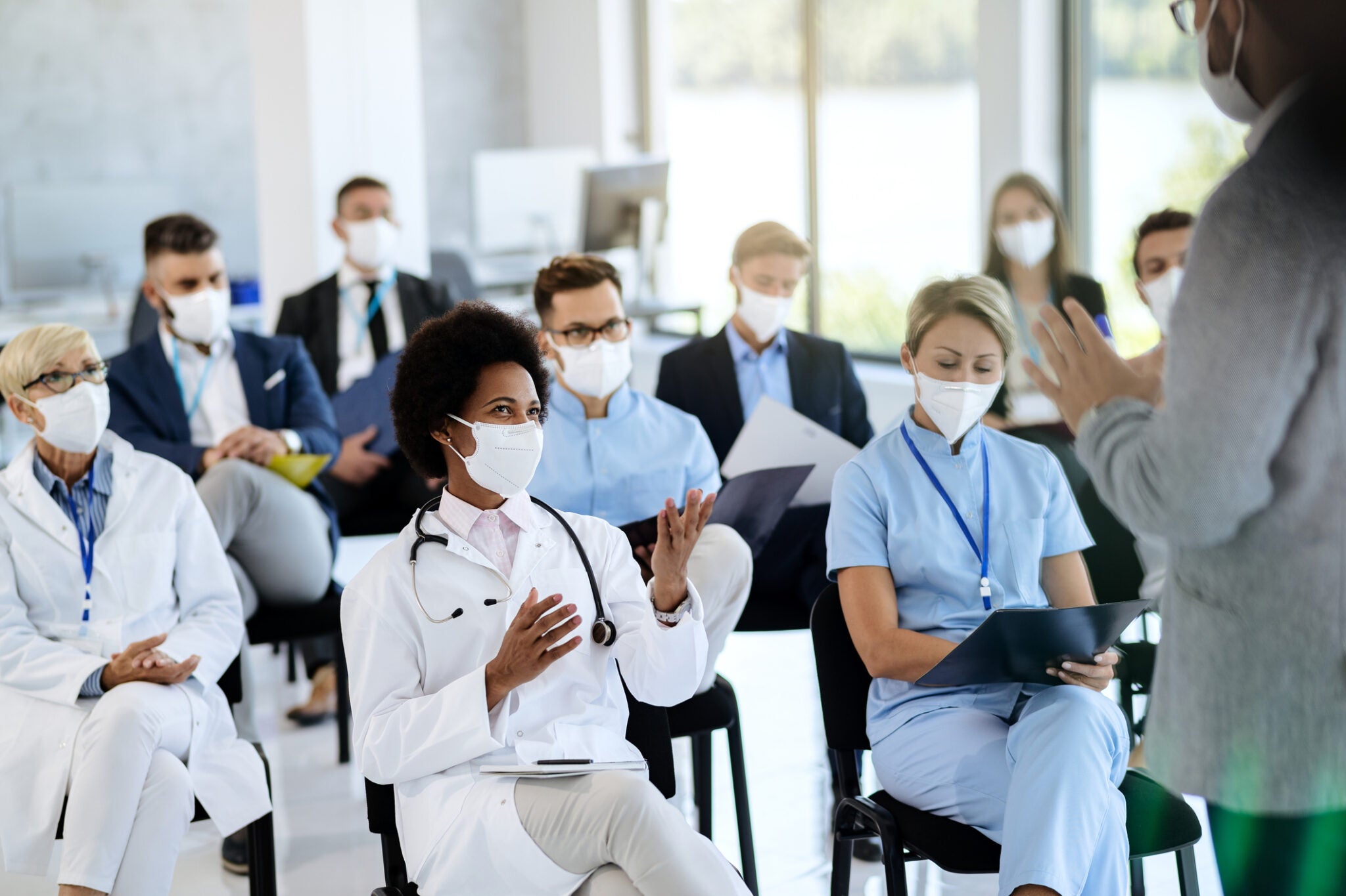 Happy black healthcare worker wearing protective face mask communicating with a businessman who is holding educational event at convention center.