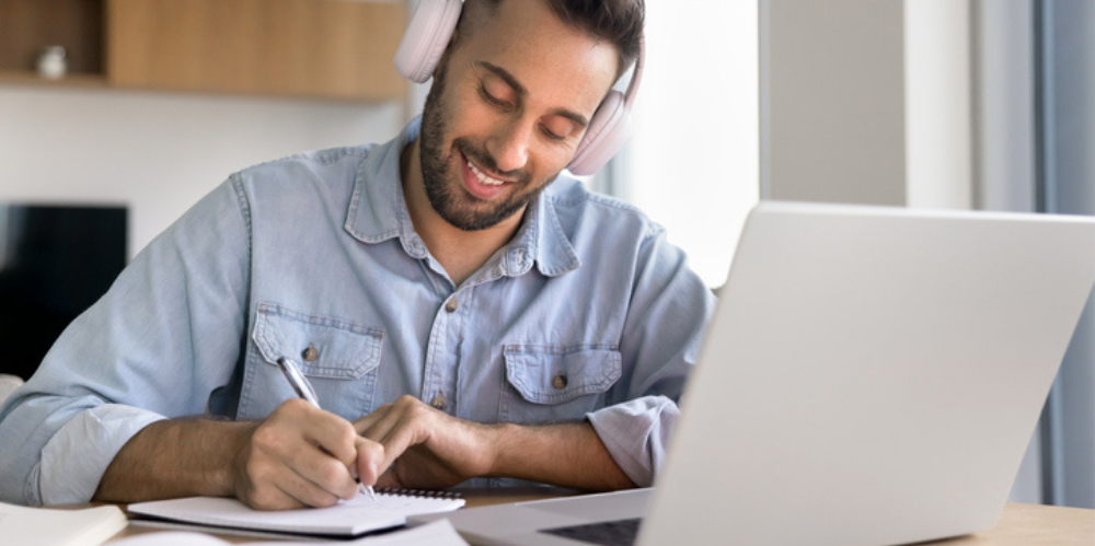 Hispanic student wearing headphones, watching online lecture and taking notes