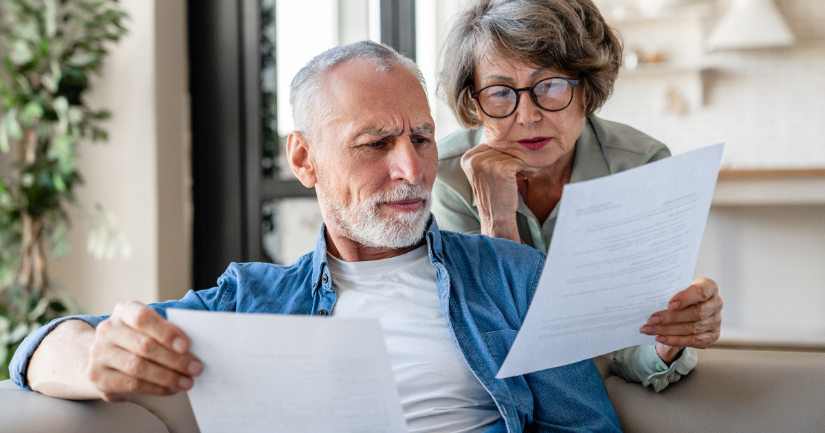 Elderly spouses reviewing paperwork together at home.