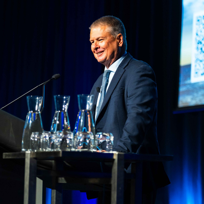 Rade Musulin presenting at the 2026 All Actuaries Summit, standing at a lectern on stage with a screen visible in the background.